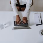 Top view of a woman typing on a laptop at a modern, minimalist home office desk with plants.
